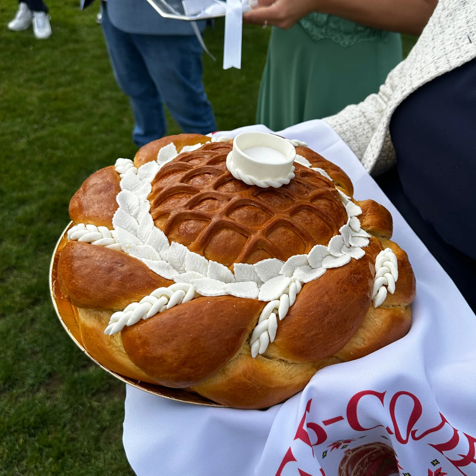 Ein Karawai mit Ährenkranz und Teigblüten auf einem bestickten Rushnyk, darauf ein kleines Salzgefäß